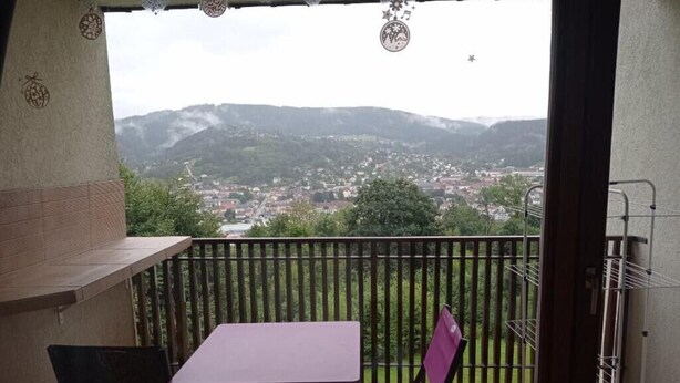 A balcony with a table and chairs, overlooking a town and hills. - Apartment on the heights of Gérardmer with a superb view (Gérardmer)