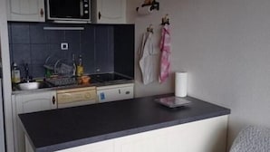 A compact kitchen with white cabinets, a microwave, and a small countertop. There is a sink with dishes and a bottle. A painting hangs on the wall above the counter. - Apartment on the heights of Gérardmer with a superb view (Gérardmer)