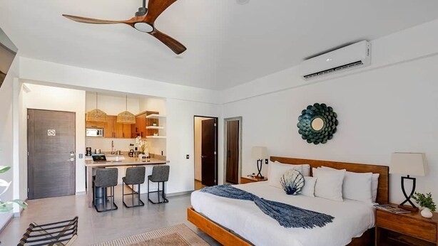 Une chambre à coucher moderne avec un lit en bois, un bureau et, au fond, un coin cuisine.