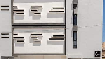 Un bâtiment moderne à la façade plate, doté de nombreuses fenêtres et comprenant un espace de stationnement avec des voitures.