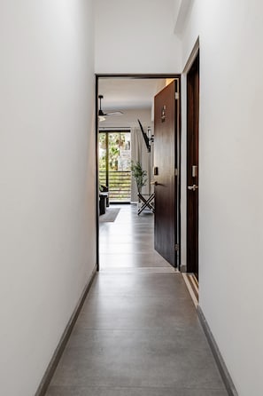 A hallway leading to a room with a door, a plant, and a staircase.