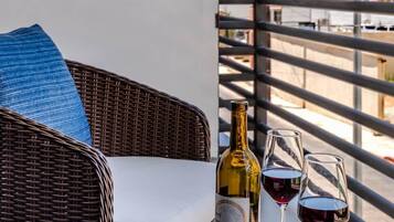 A wicker chair with a cushion, a bottle of wine, and two wine glasses on a balcony table.