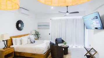 A hotel room with a bed, a television, a ceiling fan, and a view of the outdoors.