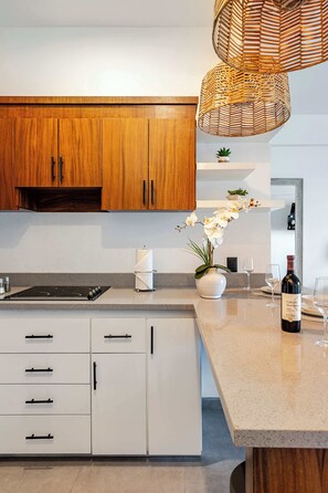A modern kitchen with wooden cabinets, a white countertop, a built-in stove, and a hanging wicker light fixture.
