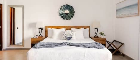 A bedroom with a wooden bed, two bedside tables, a wall-mounted air conditioner, a decorative mirror, and a painting on the wall.