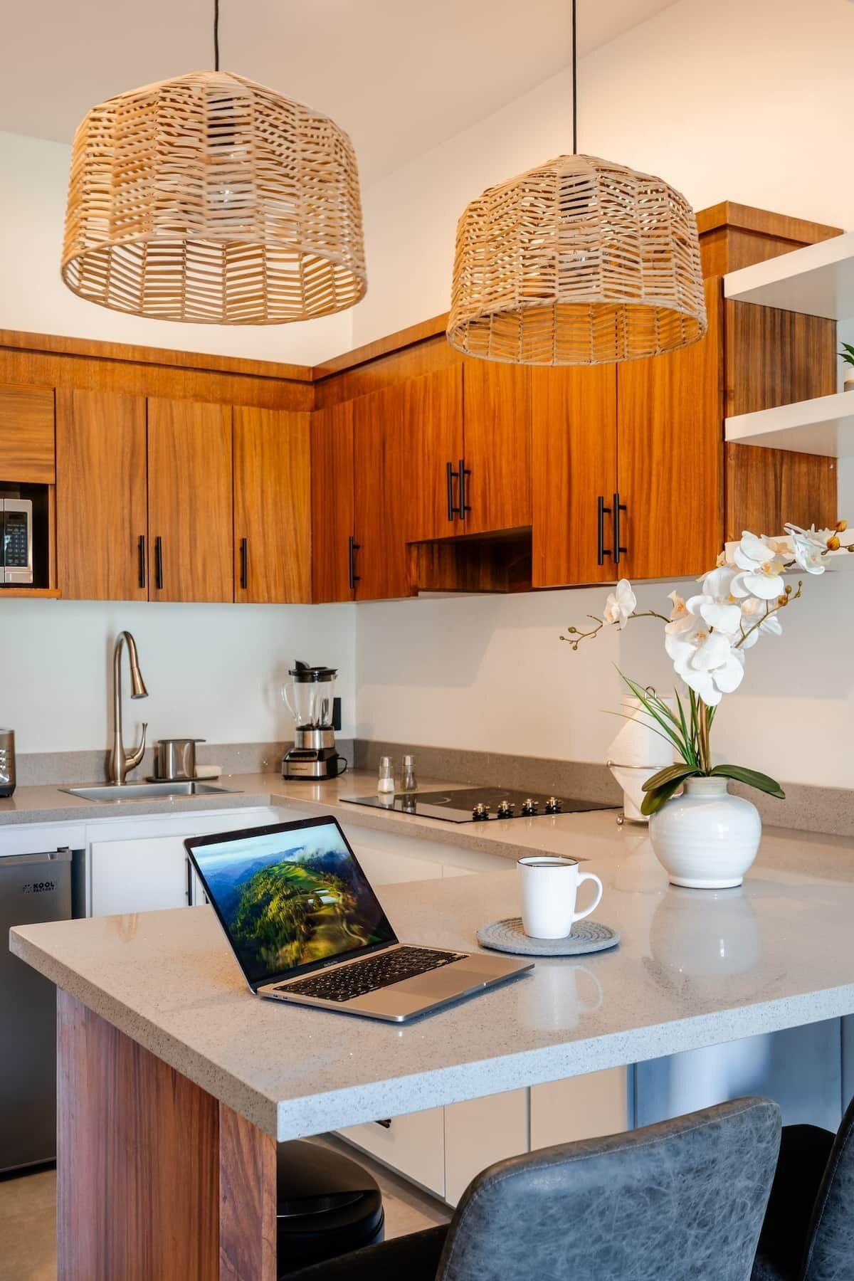 Een moderne keuken met houten kastjes, een inbouw eiland, een laptop, een koffiekop en een vaas met bloemen.