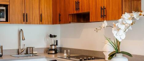 A modern kitchen with wooden cabinets, a built-in island, a laptop, a coffee cup, and a vase with flowers.