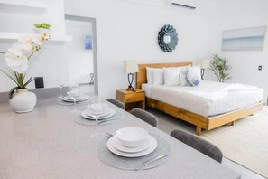 A modern bedroom with a wooden bed, white bedding, a bedside table with a lamp, and a wall-mounted mirror.