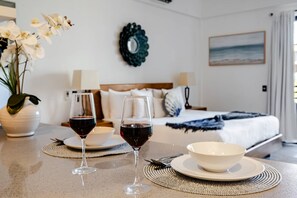 A room with a bed, two wine glasses on a table, a bowl, and a vase with flowers. - 🔥 NEW Listing | Walk to Marina & Downtown Cabo | King Bed (Cabo San Lucas)