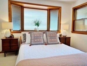 Un dormitorio con una cama grande, dos mesitas de noche con lámparas y una ventana con persianas.