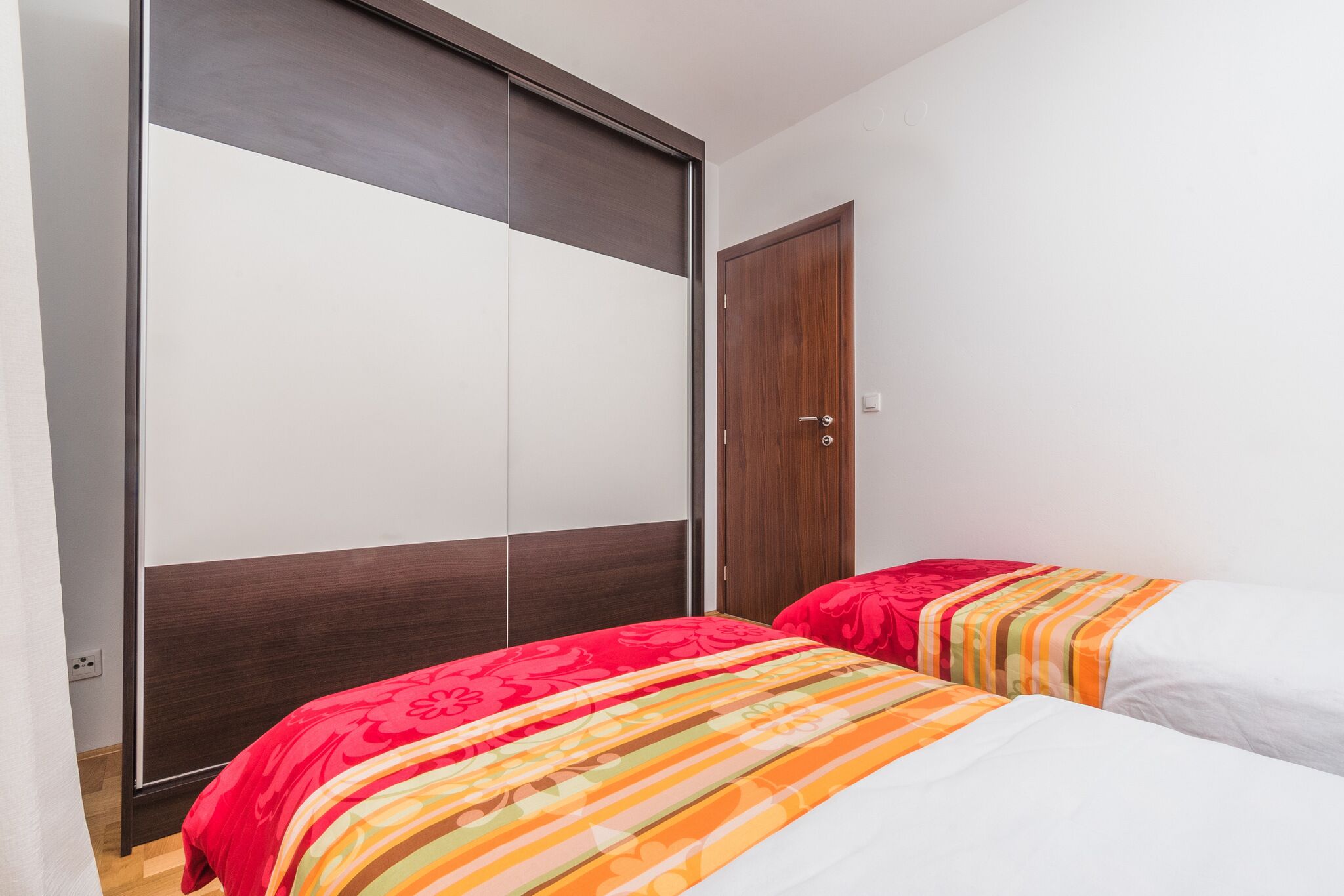 A bedroom with two beds, a wardrobe, and a wooden door.