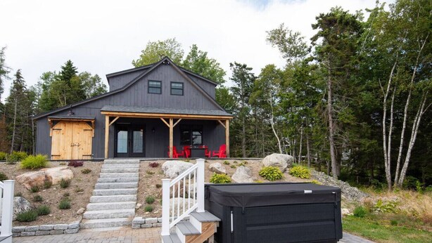 Una casa moderna con terraza de madera, porche cubierto y un calentador exterior grande y negro.