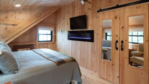 Un dormitorio acogedor en el ático, con una cama, un televisor montado en la pared y un armario.