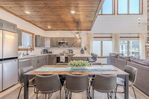 A modern kitchen with stainless steel appliances, a dining area with a wooden table, and a cozy seating area with a sofa.