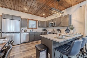 Une cuisine moderne dotée d’appareils électroménagers en acier inoxydable, d’un plafond en bois et d’un îlot central avec des tabourets de bar.