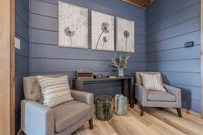 A room with two grey armchairs, a small table with chess and books, and a wall-mounted thermostat.