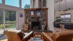 A cozy living room with a stone fireplace, leather armchairs, and a view of the outdoors.