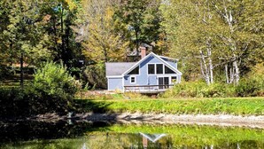 A house with a gabled roof, a front porch, and a reflection in a pond.