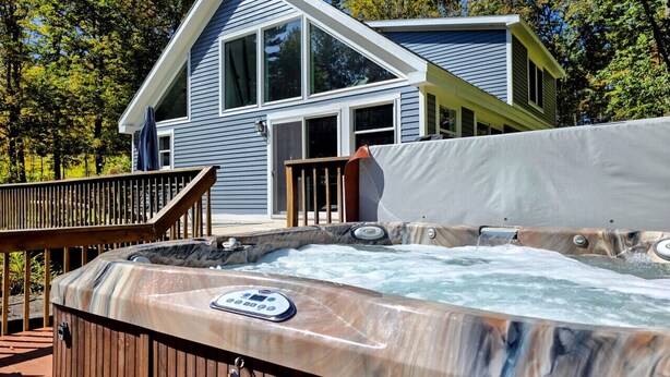 A hot tub in front of a house with a deck and a wooden railing.