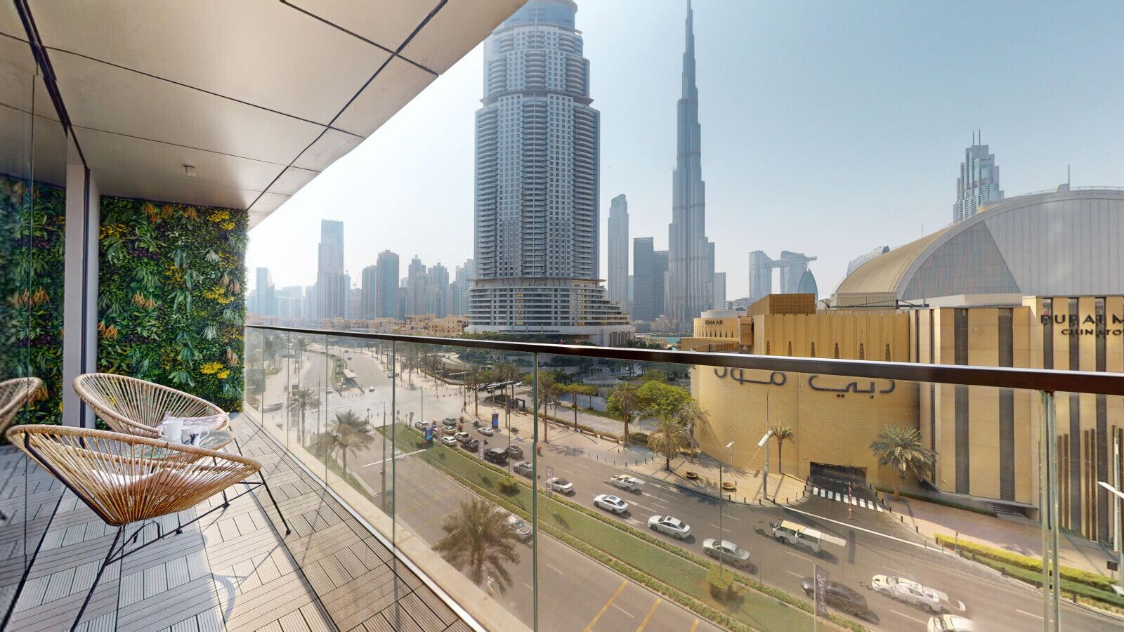 Un balcón con sillas de mimbre, vista del paisaje urbano que incluye el Burj Khalifa y un edificio con un letrero grande.