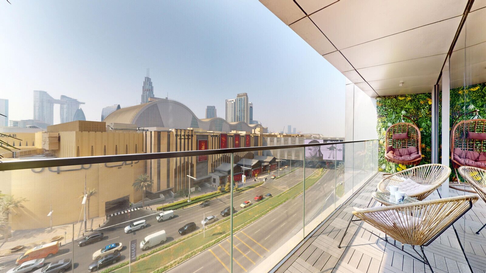 A balcony with wicker chairs, a glass railing, and a view of a cityscape with modern buildings.