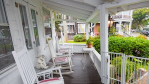 A covered porch with white rocking chairs, a small table, and a potted plant.