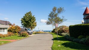 A residential street with a parked van, a house with a red roof, and a clear blue sky.