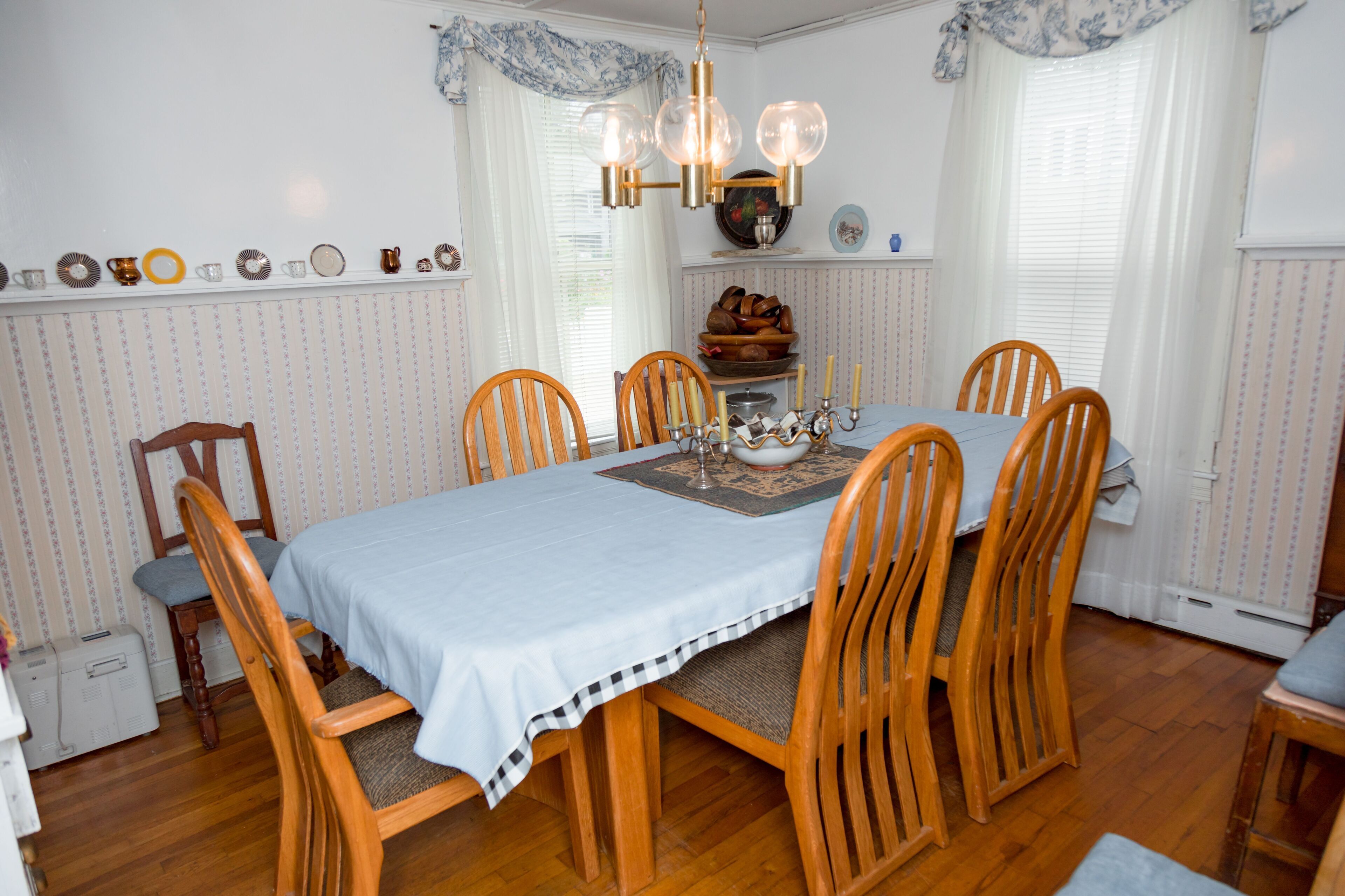 A dining room with a wooden table set for six, surrounded by six wooden chairs.