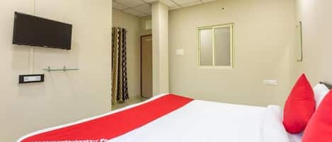 A hotel room with a bed, a television mounted on the wall, and a window.