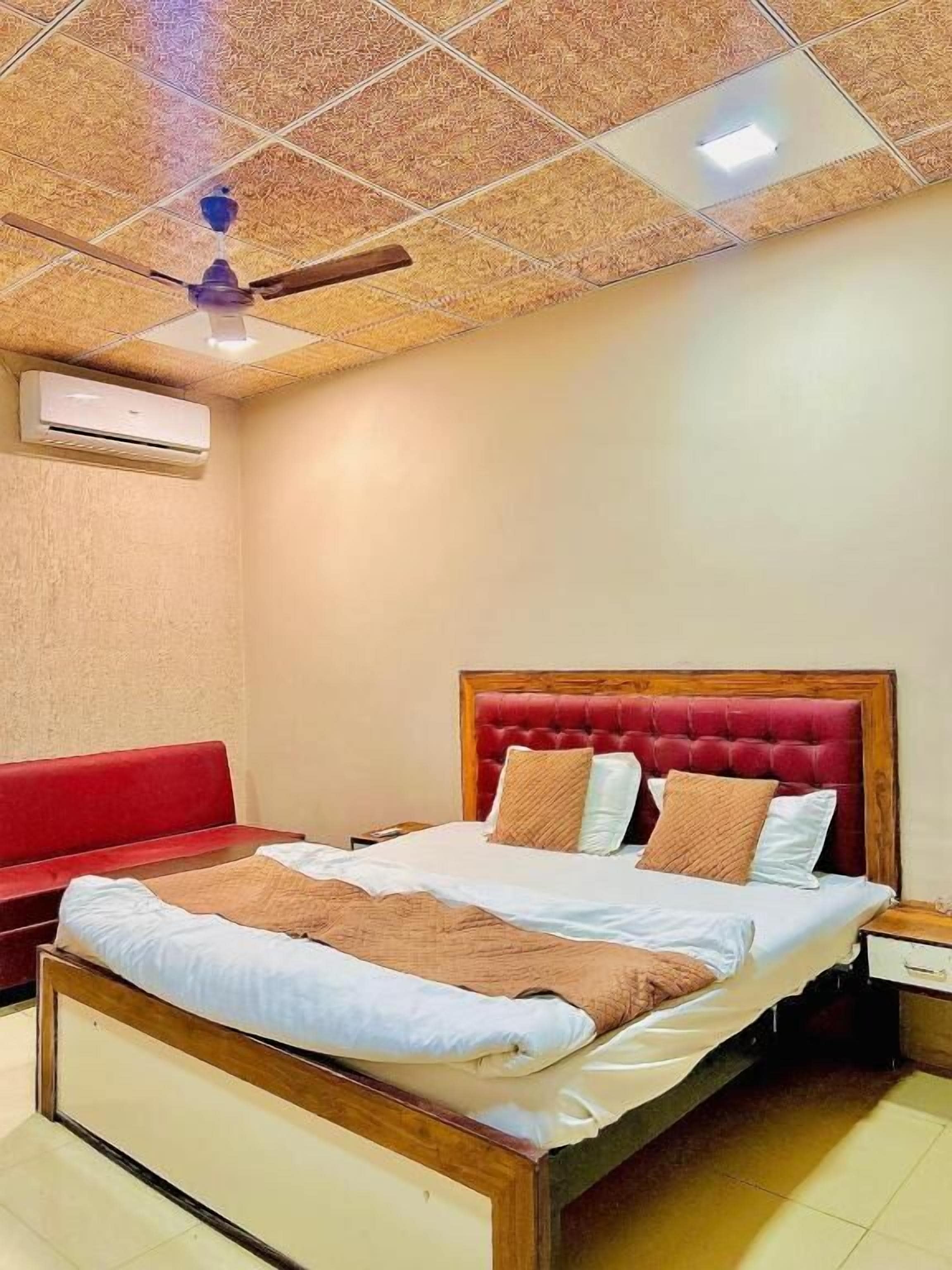 Quarto de hotel com cama, sofá vermelho, ventoinha no teto e aparelho de ar condicionado.
