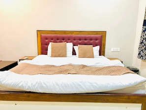 A neatly made bed with a wooden headboard, white bedding, and two beige pillows. - Hotel Jagtara (Indore)