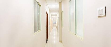 A corridor with doors on both sides, a light-colored floor, and a ceiling with recessed lighting.