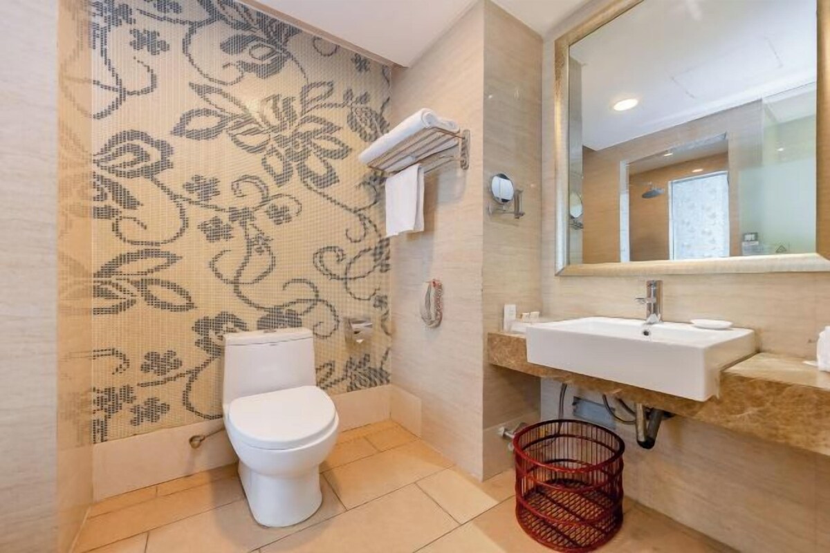 A bathroom with a toilet, sink, mirror, and patterned wall.