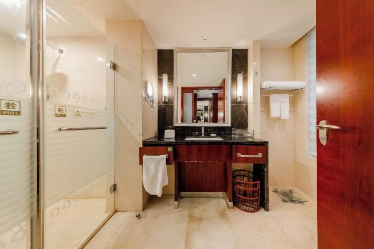 A bathroom with a glass shower enclosure, a wooden vanity with a mirror, and a towel rack.