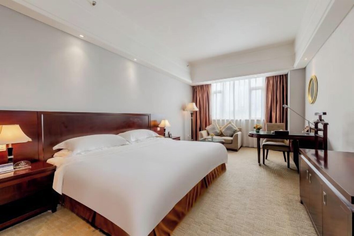 A hotel room with a large bed, a desk, a chair, and a television.