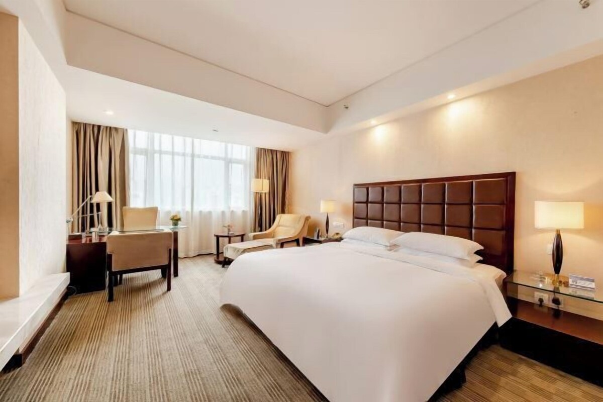 A hotel room with a large bed, a desk, two chairs, and a nightstand with lamps.