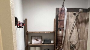 Baño pequeño con inodoro, ducha y estantes con artículos de aseo.
