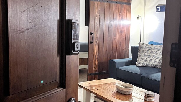 Una puerta de madera que da a una sala de estar con un sofá, una mesa de centro y un televisor en la pared.