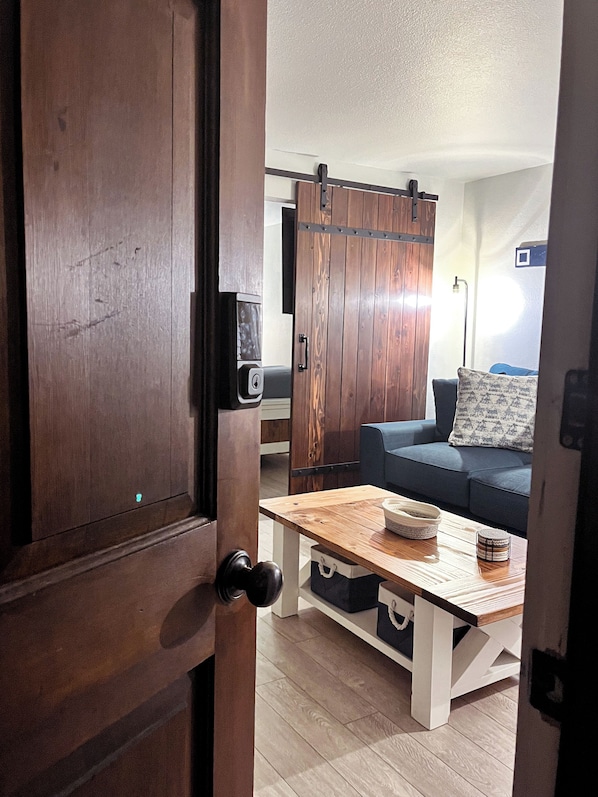 Una puerta de madera que da a una sala de estar con un sofá, una mesa de centro y un televisor en la pared.