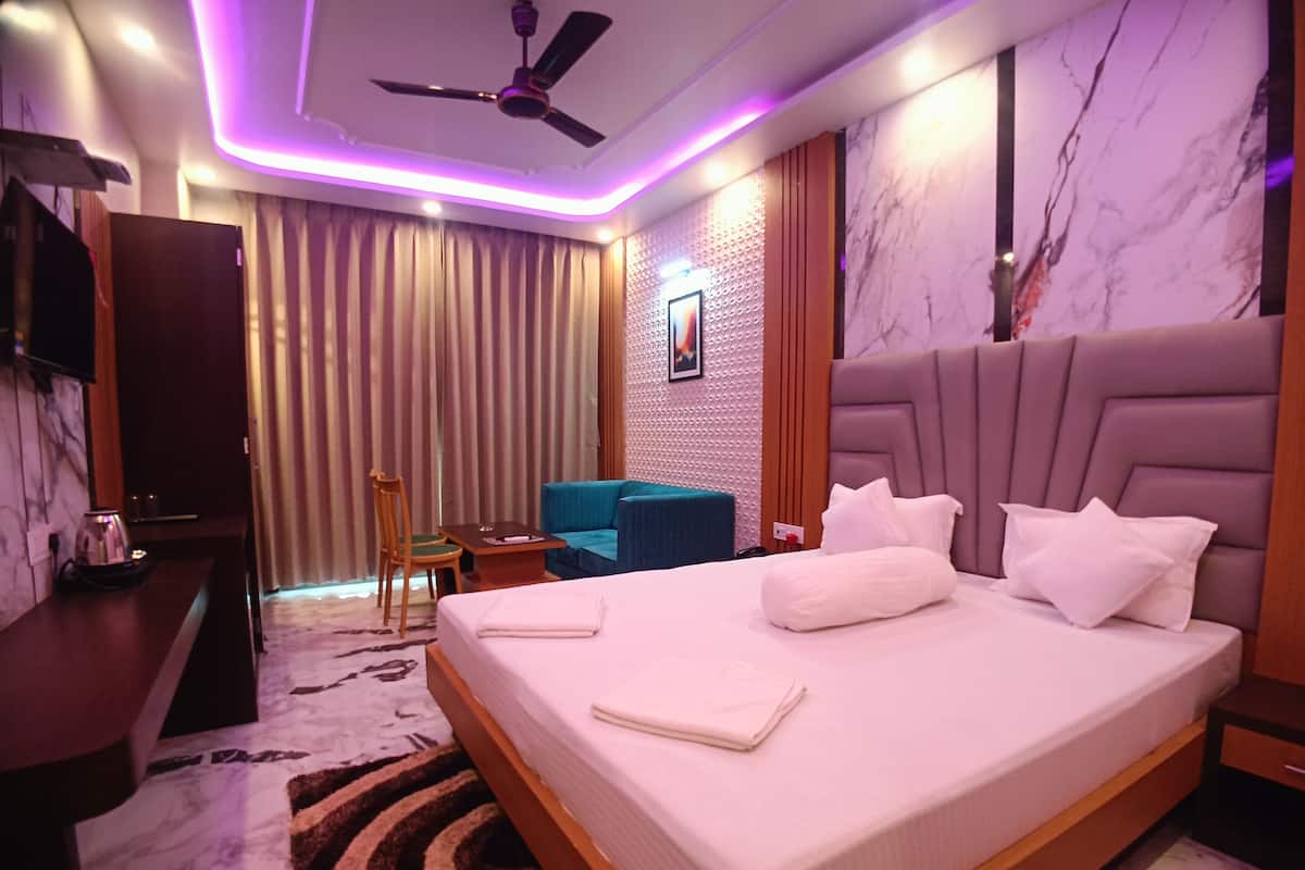 Una habitación de hotel moderna con una cama grande, ventilador de techo, televisor, escritorio y una zona de estar con una silla y una mesita.