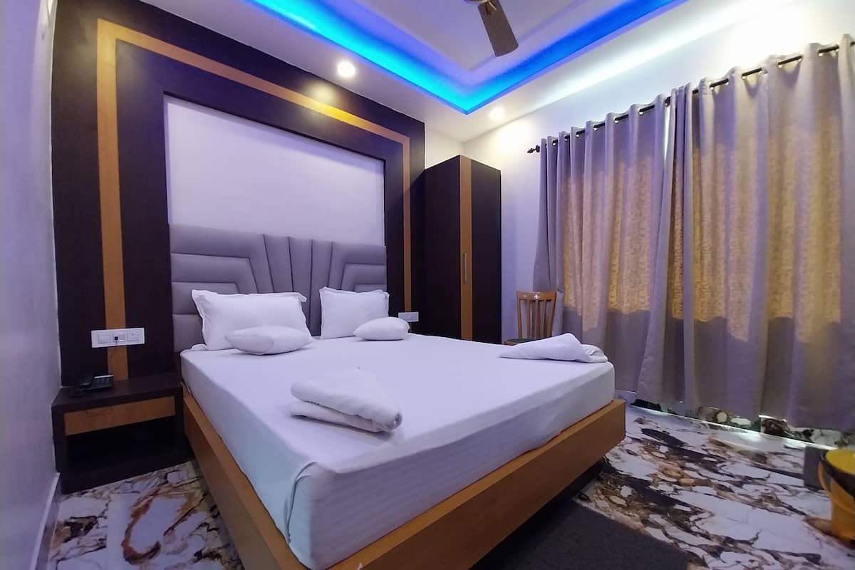 Una habitación de hotel moderna con una cama grande, cabecero, mesita de noche, una silla de madera y un ventilador de techo.