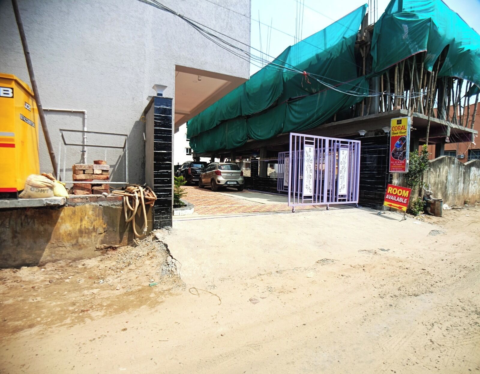 A construction site with a partially built structure, a gated entrance, and a sign indicating a room is available.