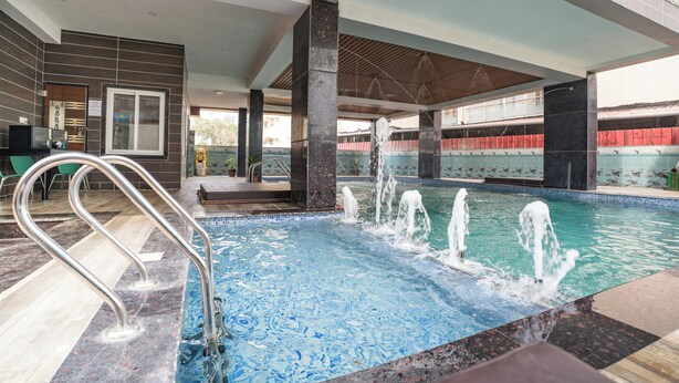 An indoor swimming pool with a tiled floor, a metal pool ladder, and a view of the outside.