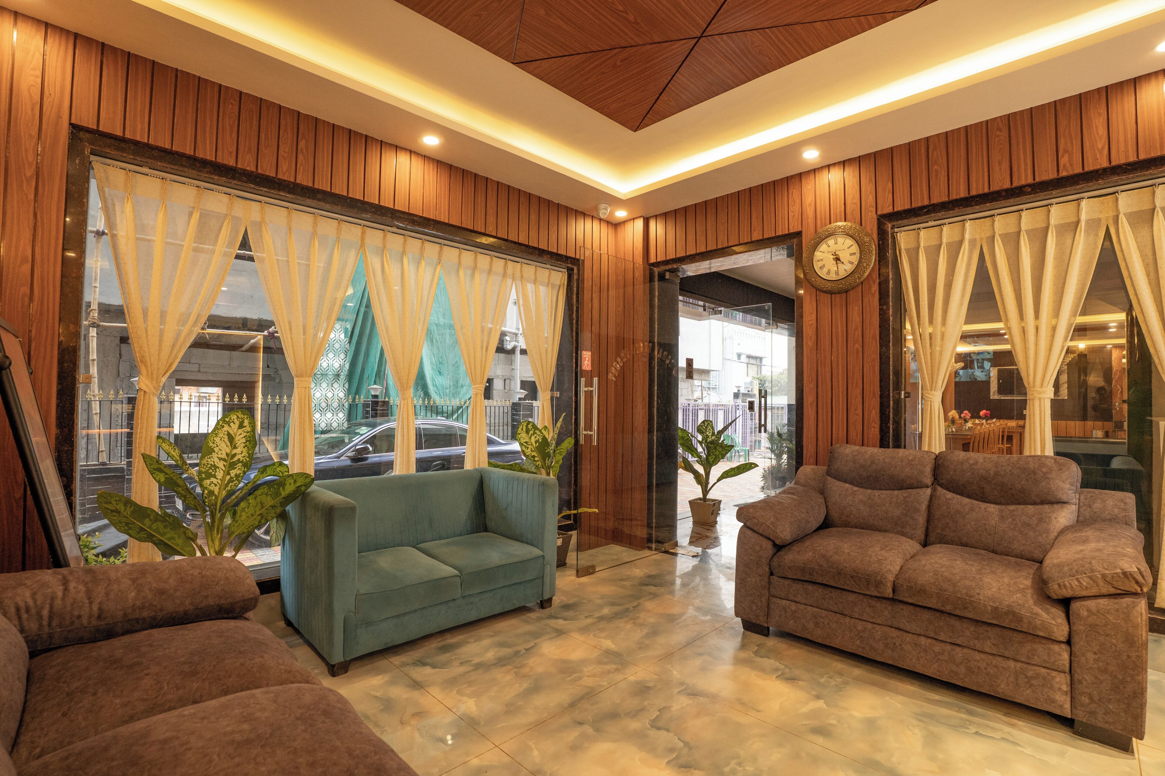 Un vestíbulo de hotel con paneles de madera, dos sofás, ventanas grandes con cortinas y un reloj en la pared.