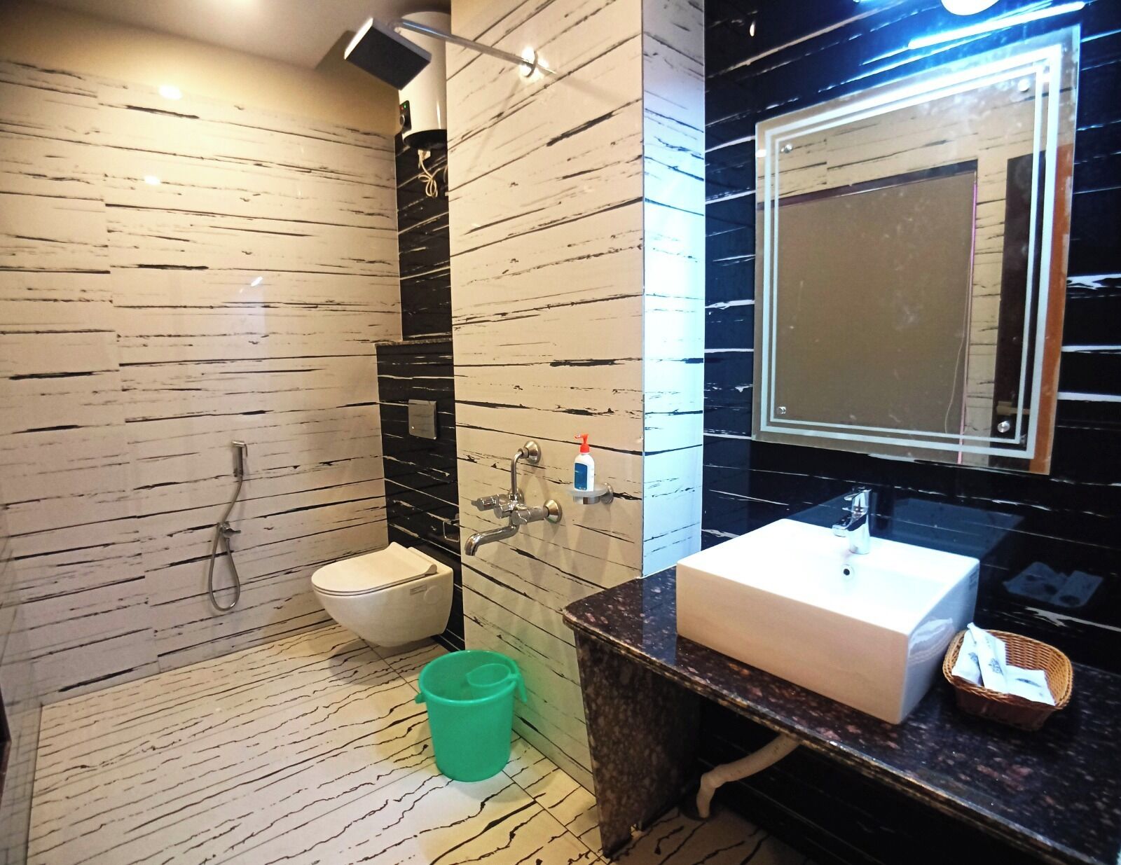 Ein modernes Badezimmer mit Marmorboden, Toilette, Waschbecken und einem Spiegel sowie einem grünen Eimer.