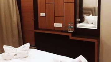 Een hotelkamer met een bed, een houten garderobe, een spiegel en een handdoek op het bed.