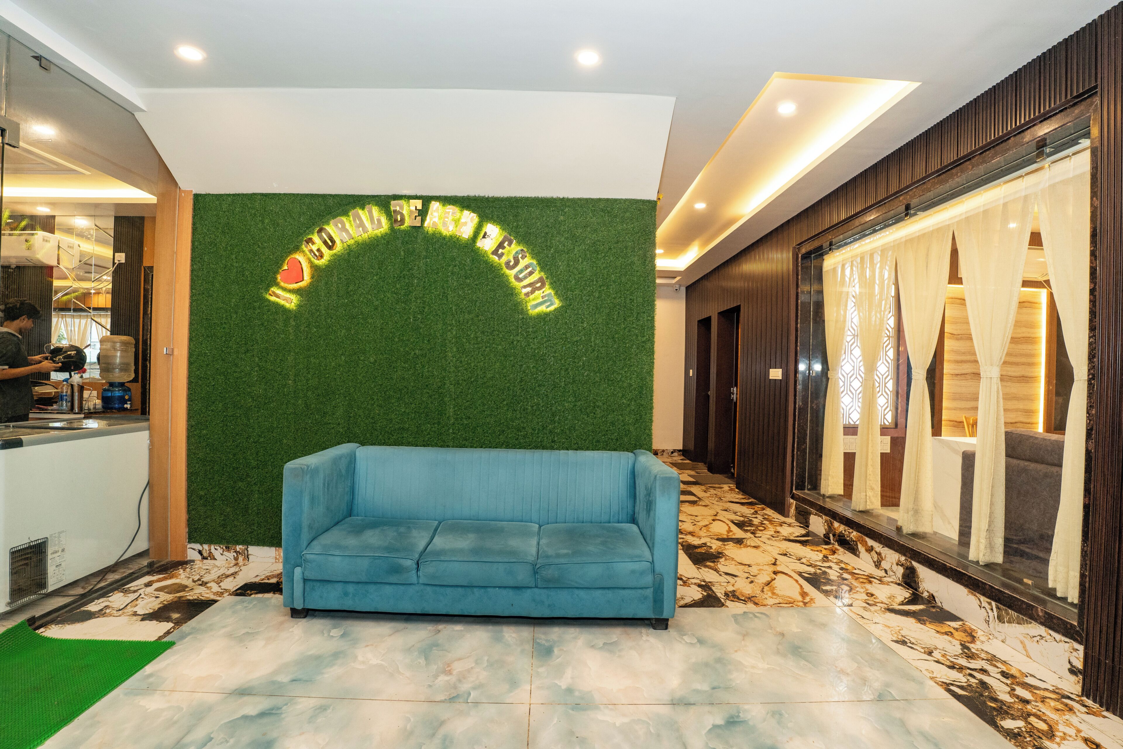 A reception area with a green wall, a blue sofa, and a sign that reads 'Gorbe Beach Resort.'