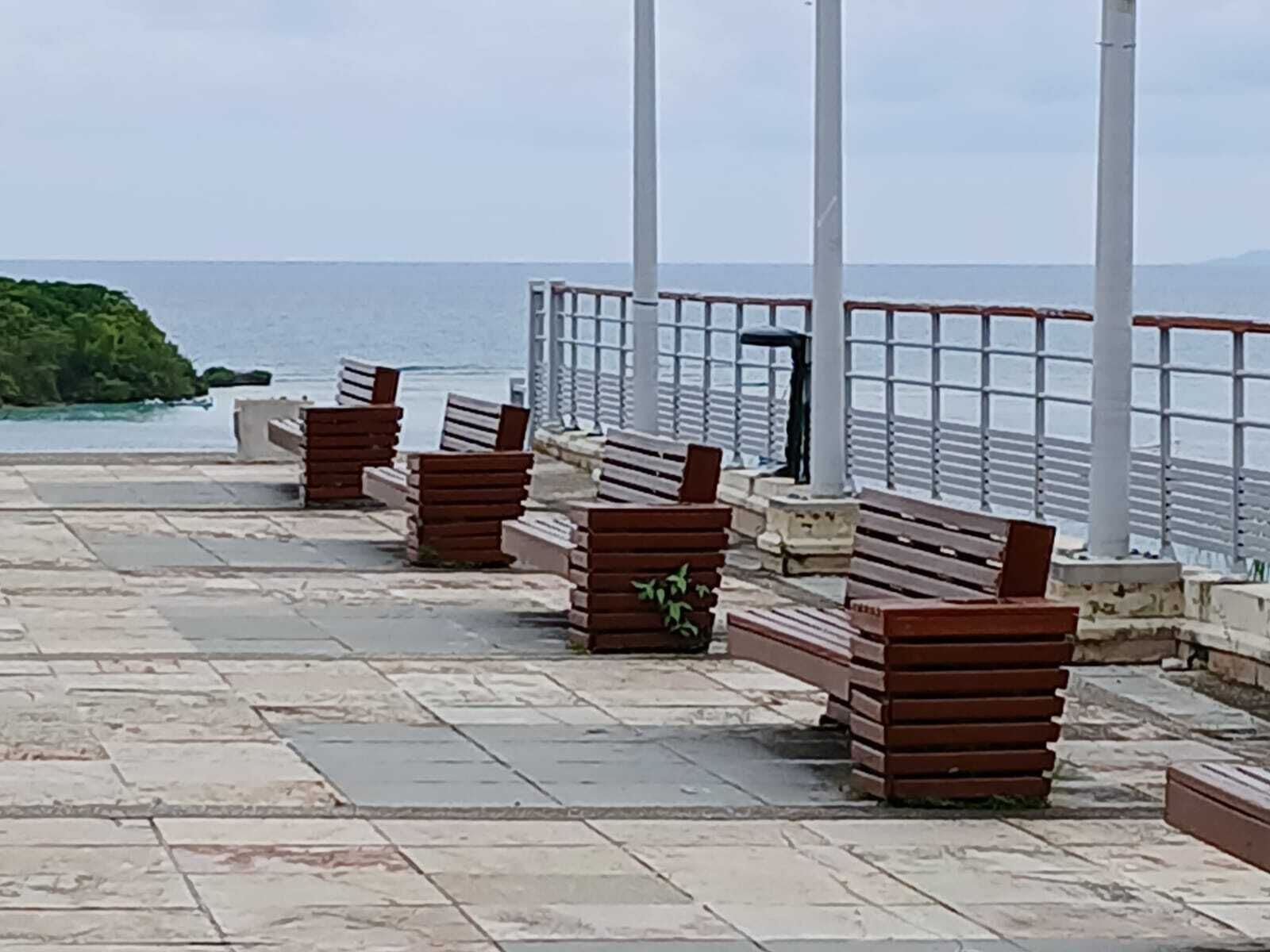 A seaside promenade with benches and a railing overlooking the ocean.