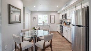 A modern kitchen with a central island, stainless steel appliances, and a dining area with a glass table and cushioned chairs.