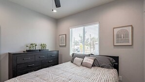 A bedroom with a bed, a dresser, a window with blinds, and two framed pictures on the wall.